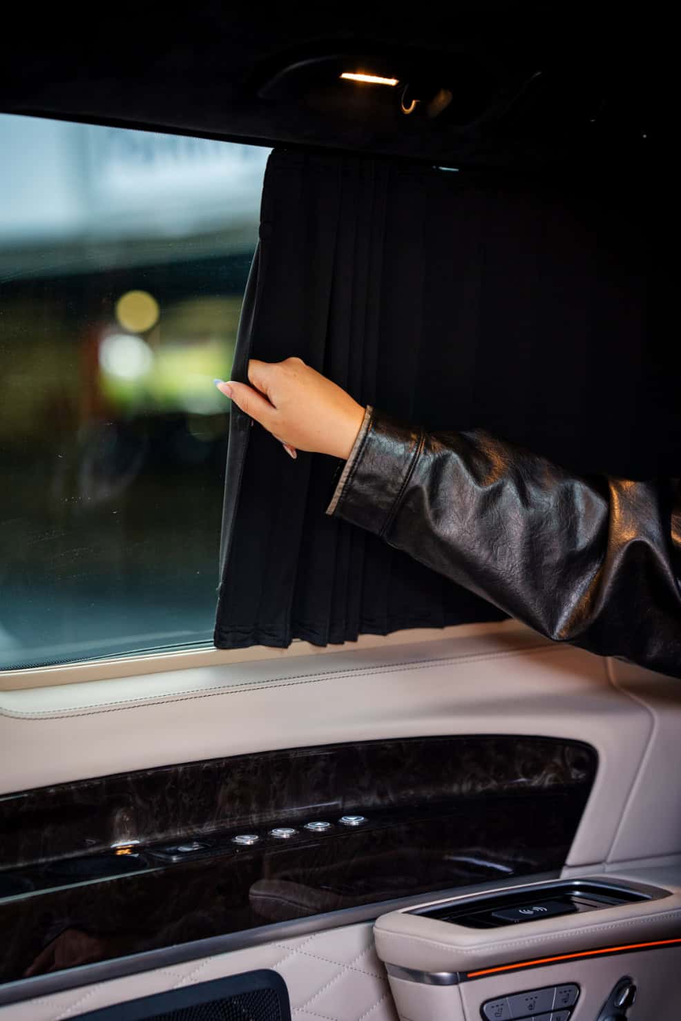 Swift Luxury Travel-58 Passenger adjusting window shade in luxury vehicle for travel comfort.